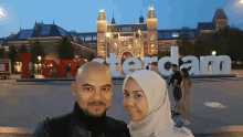 a man and a woman are posing in front of a sign that says amsterdam