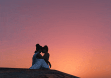 a couple sitting on a rock at sunset