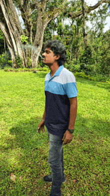 a man in a blue and white shirt is smoking a cigarette in front of a tree