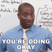 a man in a blue shirt and tie says " you 're doing okay " in front of a white board