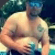 a shirtless man wearing sunglasses is standing next to a swimming pool holding a can of beer .