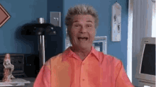 a man in an orange shirt is making a funny face in front of a computer screen .