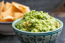 a bowl of guacamole sits in front of a bowl of tortilla chips