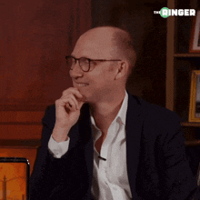 a bald man wearing glasses and a suit is sitting in front of a bookshelf with the ringer written above him