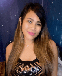 a woman wearing a black top with sequins and a heart necklace smiles for the camera