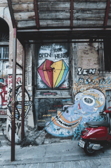 a red scooter is parked in front of a graffiti covered door that says " open heart "