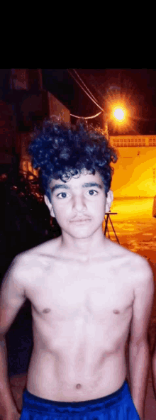 a shirtless young man with curly hair is standing in front of a street light