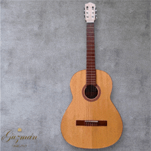 a guitar is hanging on a gray wall with the name guzman on the bottom