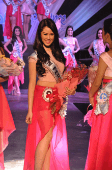 a woman in a pink dress is holding a bouquet of flowers and wearing a sash that says point fer