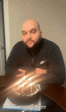 a man sitting at a table with a birthday cake with candles and the word maddox on the bottom