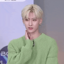 a young man wearing a green sweater and earrings is standing in a room .