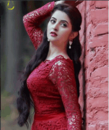 a woman in a red dress is leaning against a brick wall