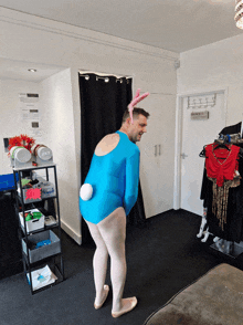 a man in a blue leotard and bunny ears stands in a room with a sign that says dance