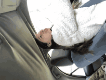 a woman in a white jacket is laying on her back in the back seat of a car