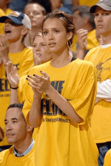 a woman wearing a yellow nike shirt applauds while watching a game