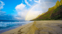 a rainbow is visible over the ocean and mountains on a beach .