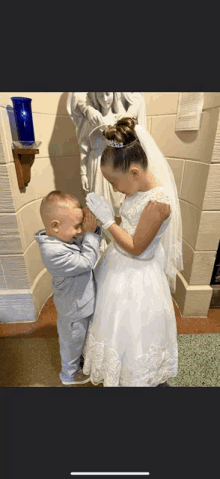 a little girl in a wedding dress and a little boy in a suit are praying together