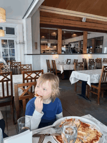 a little boy sitting at a table with a plate of pizza and a glass of water