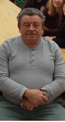 a man wearing a gray shirt and a ring sits with his hands folded