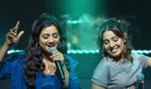 two women singing into microphones in front of a green light