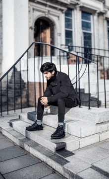 a man in a black jacket sits on a set of steps