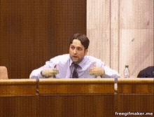 a man in a suit and tie is sitting at a desk with a bottle of water in front of him ..