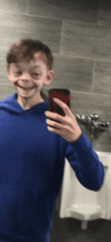 a young boy is taking a selfie in a public restroom .