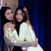 two women hugging each other in front of a blue curtain