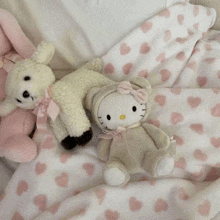 two stuffed animals , a bunny and a hello kitty , are sitting on top of a pink heart blanket .