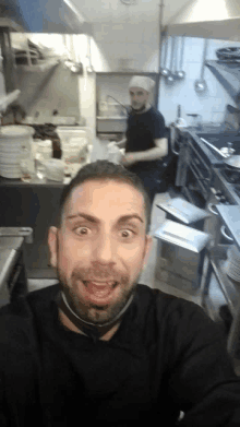 a man is taking a selfie in a kitchen while another man prepares food