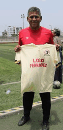 a man in a red shirt is holding a white soccer jersey with the name logo fernandez on it .