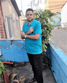 a man wearing a blue shirt and black pants stands in front of a blue wall