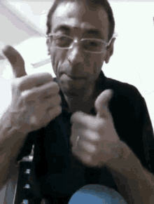 a man wearing glasses and a black shirt is giving a thumbs up