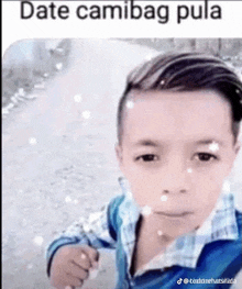 a young boy in a blue shirt is standing on a dirt road with snow falling on him .