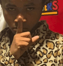 a young boy wearing a leopard print jacket is making a shhh sign with his finger .