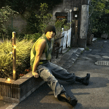 a man sits on the sidewalk wearing a green vest