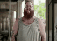 a fat man with a beard and tattoos is wearing glasses and a tank top .