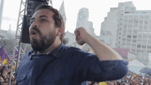 a man with a beard holds his fist up in front of a crowd with a building in the background that says aww