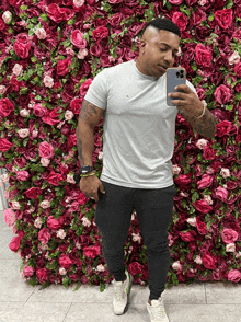 a man taking a picture of himself in front of a wall of pink roses