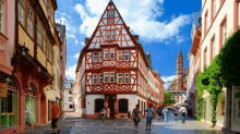 a group of people are walking down a street in front of a large building with a triangle roof .