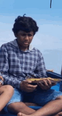 a boy in a plaid shirt is sitting on a boat holding a bowl of food .