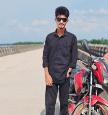 a young man wearing sunglasses and a black shirt stands next to a red motorcycle