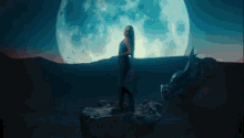 a woman stands in front of a full moon