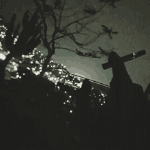 a person is holding a cross in their hand in front of a tree at night .