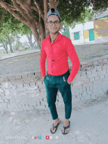 a young man wearing a red shirt and green pants stands in front of a brick wall