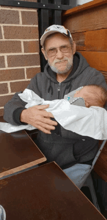 an older man is holding a baby in his arms while sitting at a table