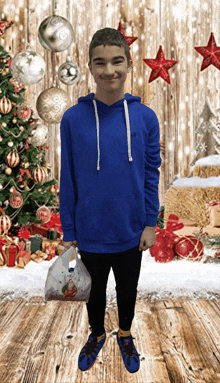 a boy in a blue hoodie is holding a bag with santa on it