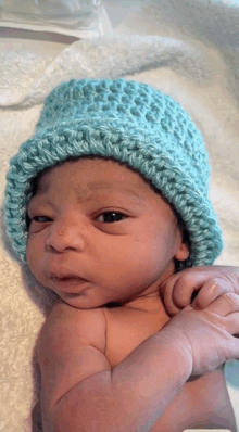 a baby wearing a blue hat is laying on a white blanket