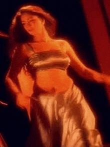 a woman in a satin crop top and a white skirt is dancing in a dark room .