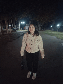 a girl in a white jacket and black pants is standing in a park at night